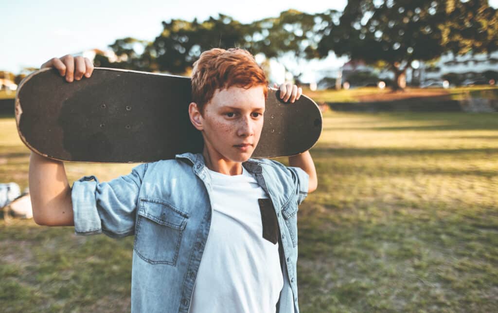 A boy holds a skateboard, appearing pensive, depicting emotional trauma in addiction