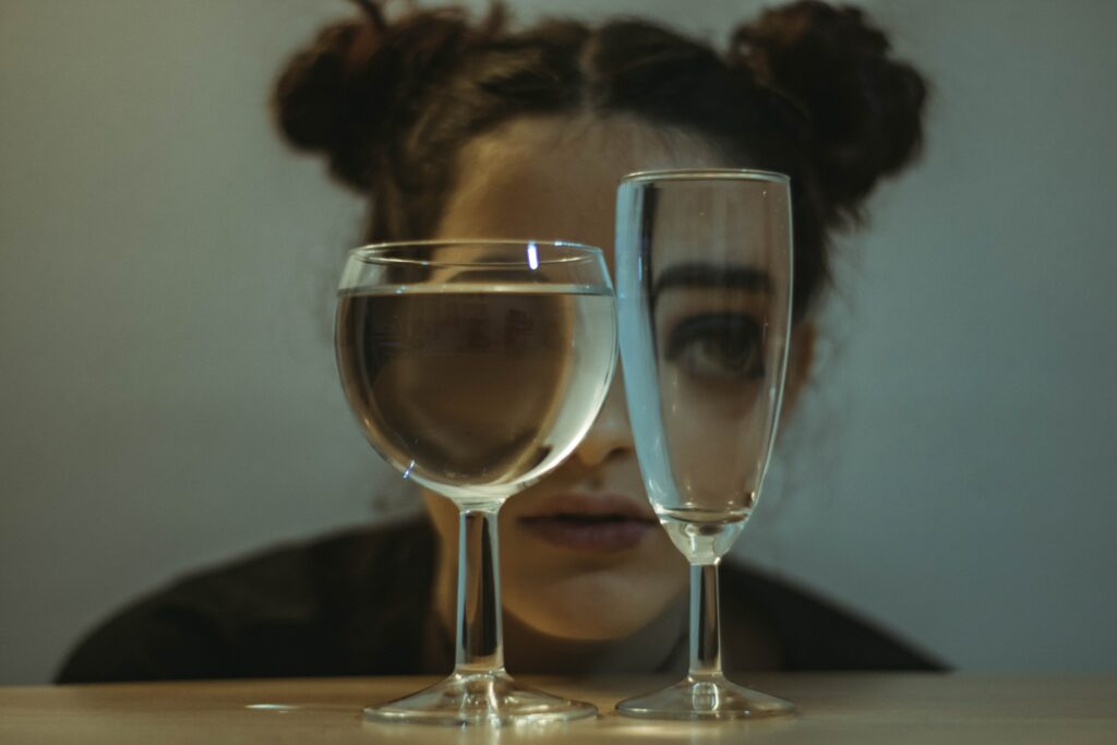 A woman's appearance is skewed as shelooks through two wine glasses, representing EtOH Abuse: Understanding Ethanol Alcohol