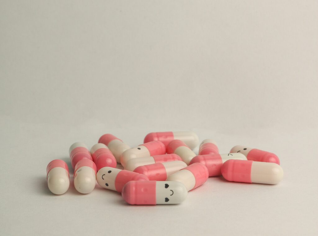 Pink and white prescription antidepressant pills sit on a white counter with smiley faces on them. 