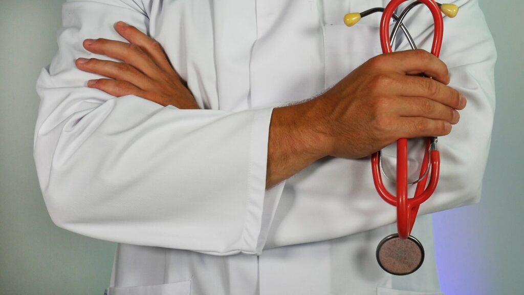 Male doctor in while coat is crossing his arms while holding a red stethoscope, presumably giving advice about the side effects of Adderall. 