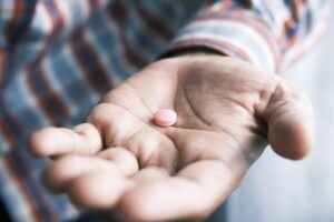 A man's hand holds a pink antidepressant pill.