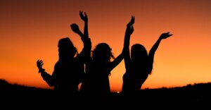Three people are shadowed with their hands up in celebration against a sunset representing best sober nightlife activities to do in newport beach california.