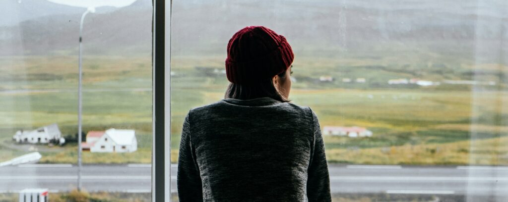 A woman in a red beanie stares out of a large window, presumably thinking about how long Percocets stay in your system.