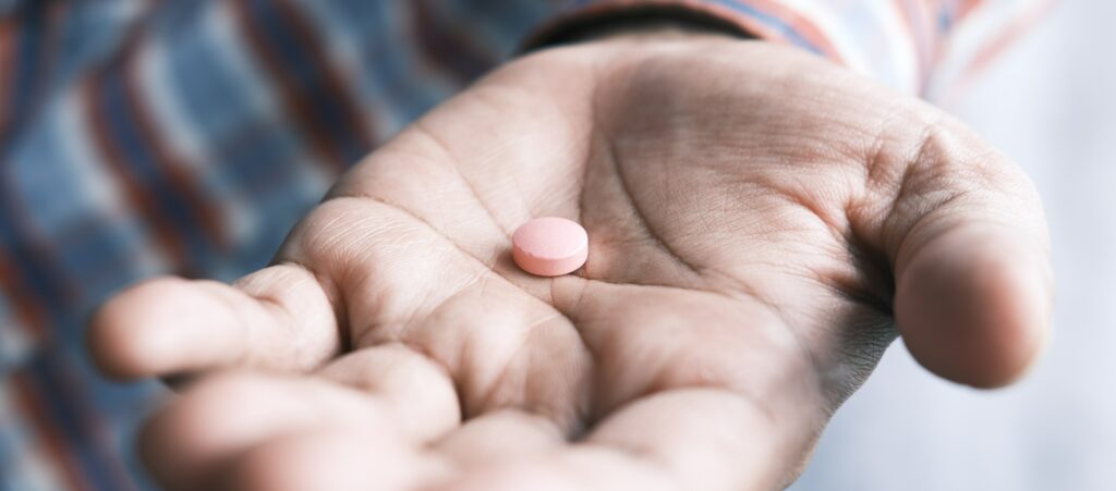 A man is holding a pink pill in his hand, presumably wondering how long does Percocet stay in your system?