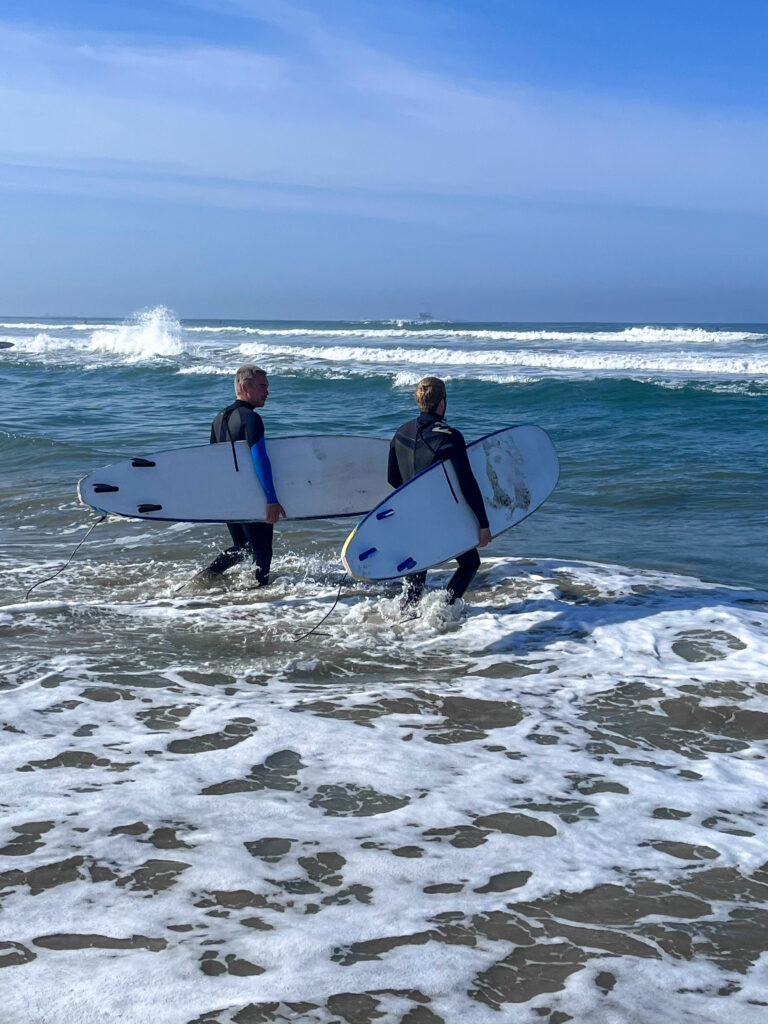 2 surfers walking into the ocean with their surfboards