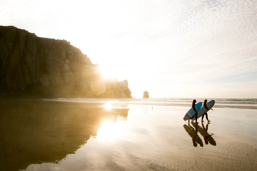 two people with surfboards walk down the beach to represent to represent a California sober lifestyle.
