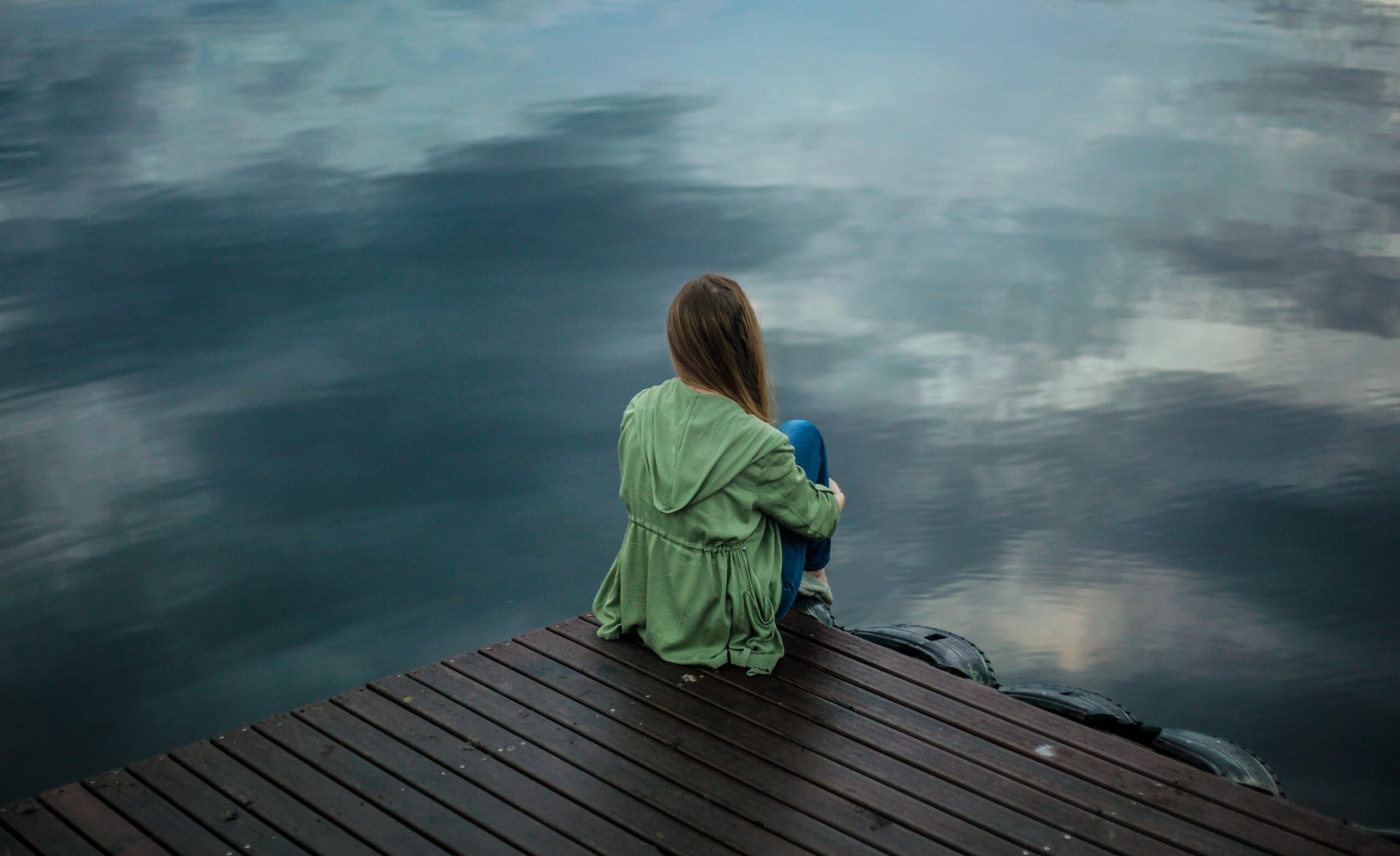 a woman sits alone looking out at a body of water to represent the side effects of hydrocodone addiction.