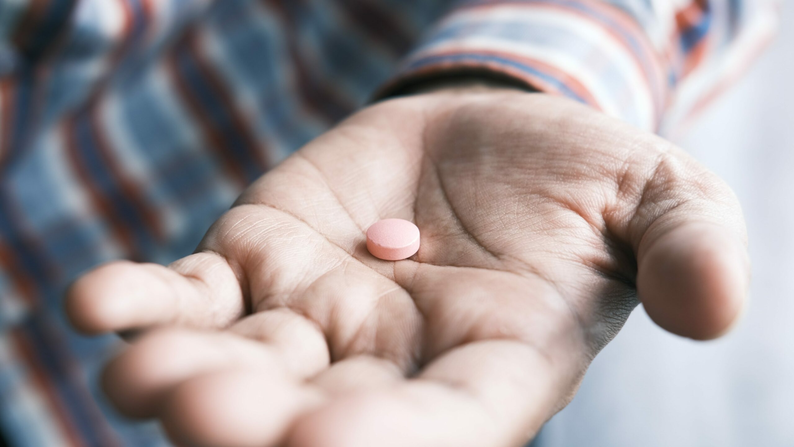 A man's hand holds a pill to represent prescription drug addiction..