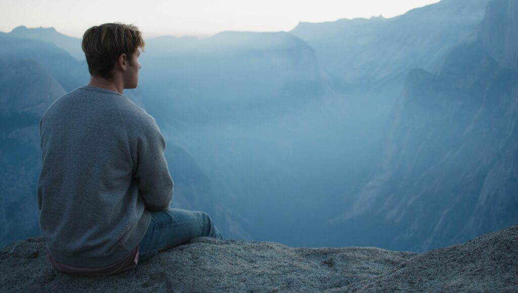 A man sits on a hill looking out at a mountain range to represent the question, "what types of drugs are barbiturates?".