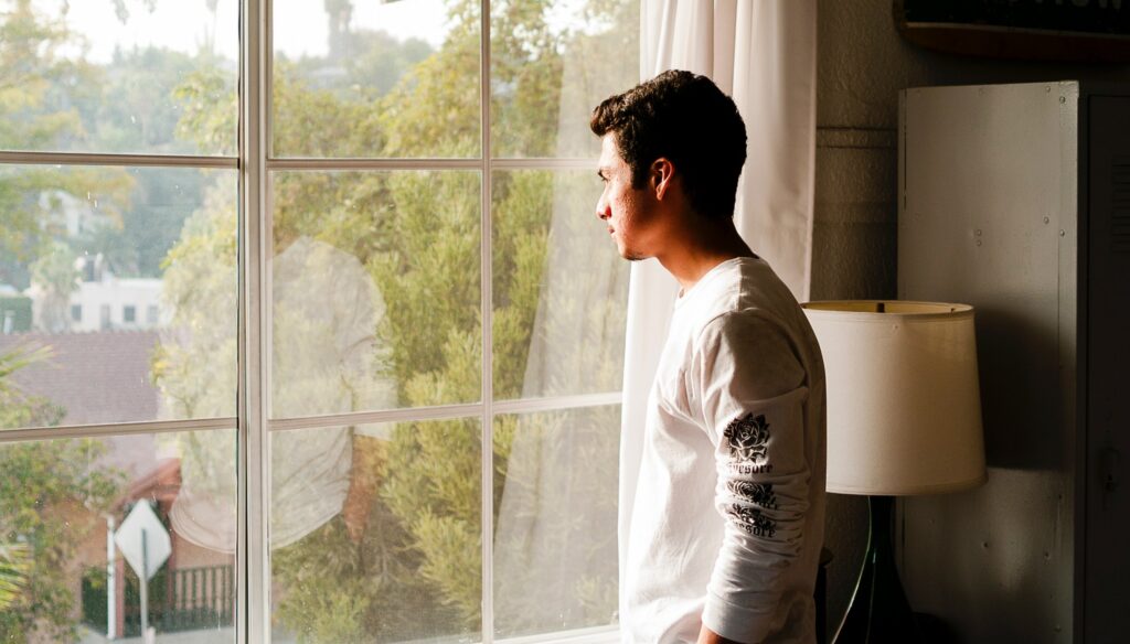 A man stands at a window looking out to represent the question how to stop drug addiction