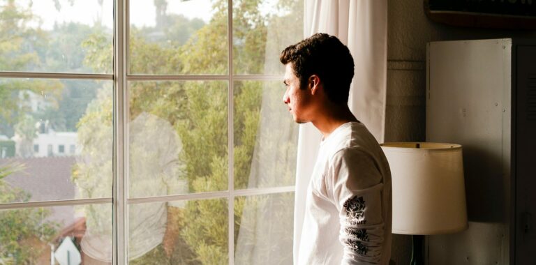 A man stands at a window looking out to represent the side effects of stopping meloxicam