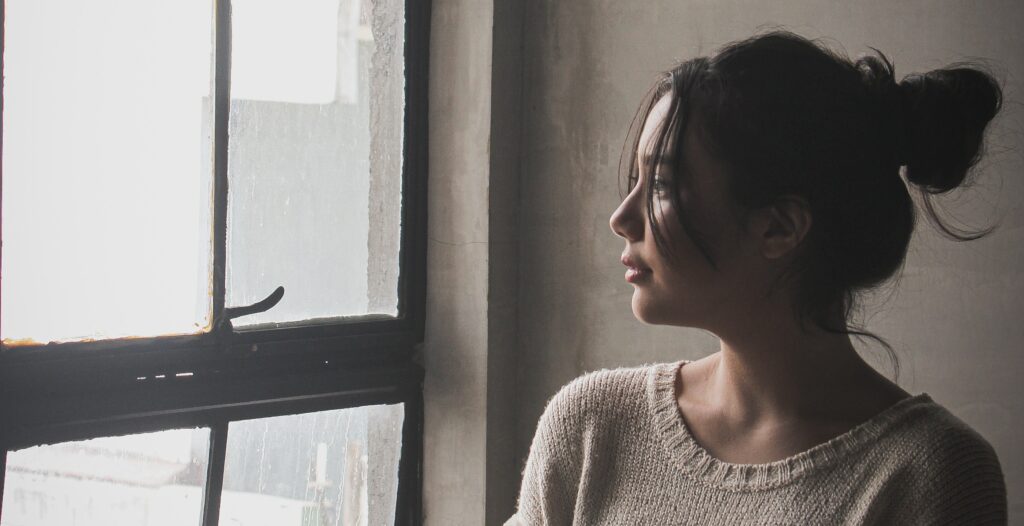 a woman looks out a window to represent thinking about treatment program, healthy boundaries, and withdrawal symptoms. 
