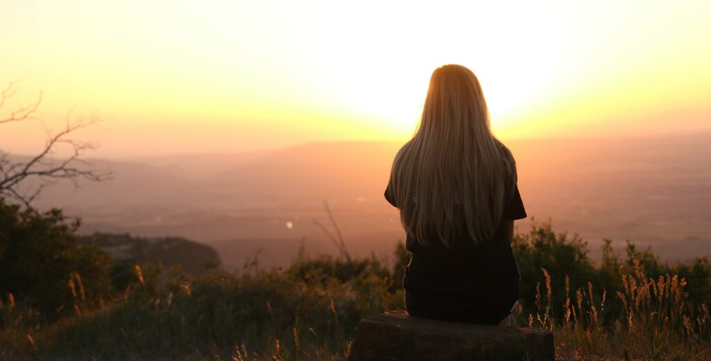A woman sits on a hill watching a sunset to represent the question, "is addiction a choice?".