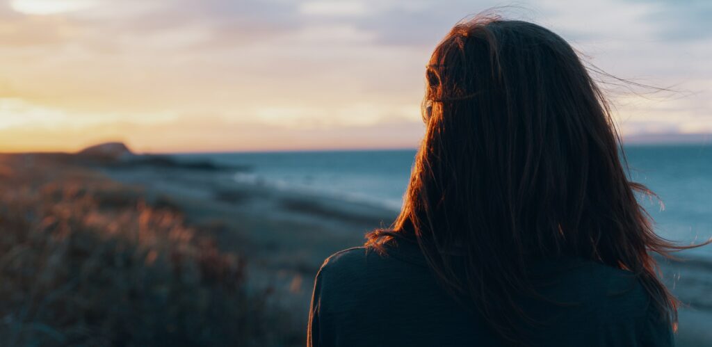 A woman looks out at a California beach at sunset to represent what is an addict